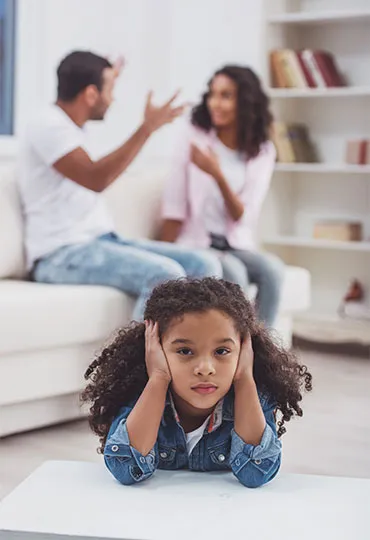 Imagen que muestra a una niña tapándose los oidos y una pareja detrás discutiendo.