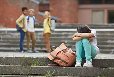 Niña llorando en la salida de una escuela con tres niños señalándola y riéndose